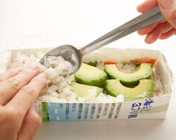 ご飯1/2量を平らに入れ、アボカドを並べる。残りのご飯を詰めてラップをかけ、牛乳パックのふたをしてご飯が箱にぴったり収まるくらいしっかりと押す。冷蔵庫で30分ほどおき、包丁を水で濡らしながら食べやすい大きさに切る。