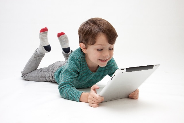 寝転がってタブレットを見る男の子