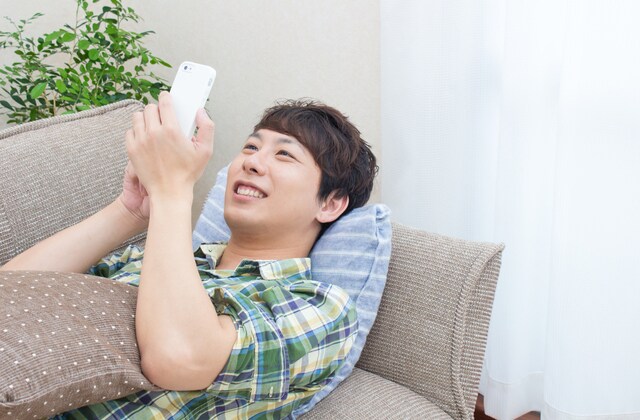 寝ながらスマートフォンをいじっている男性