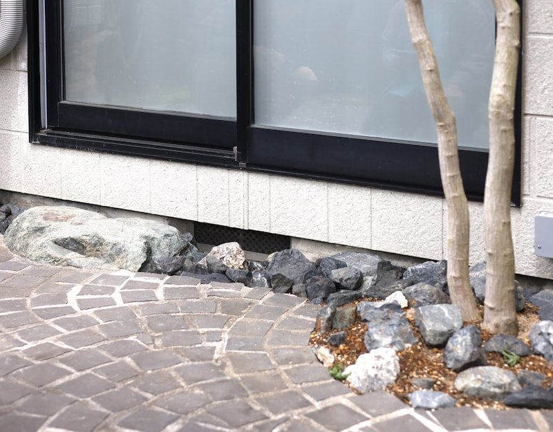 住宅窓際の足元は、沓脱石のみでなく、黒いピンコロの際をゴロタや植栽で自然風にデザイン。