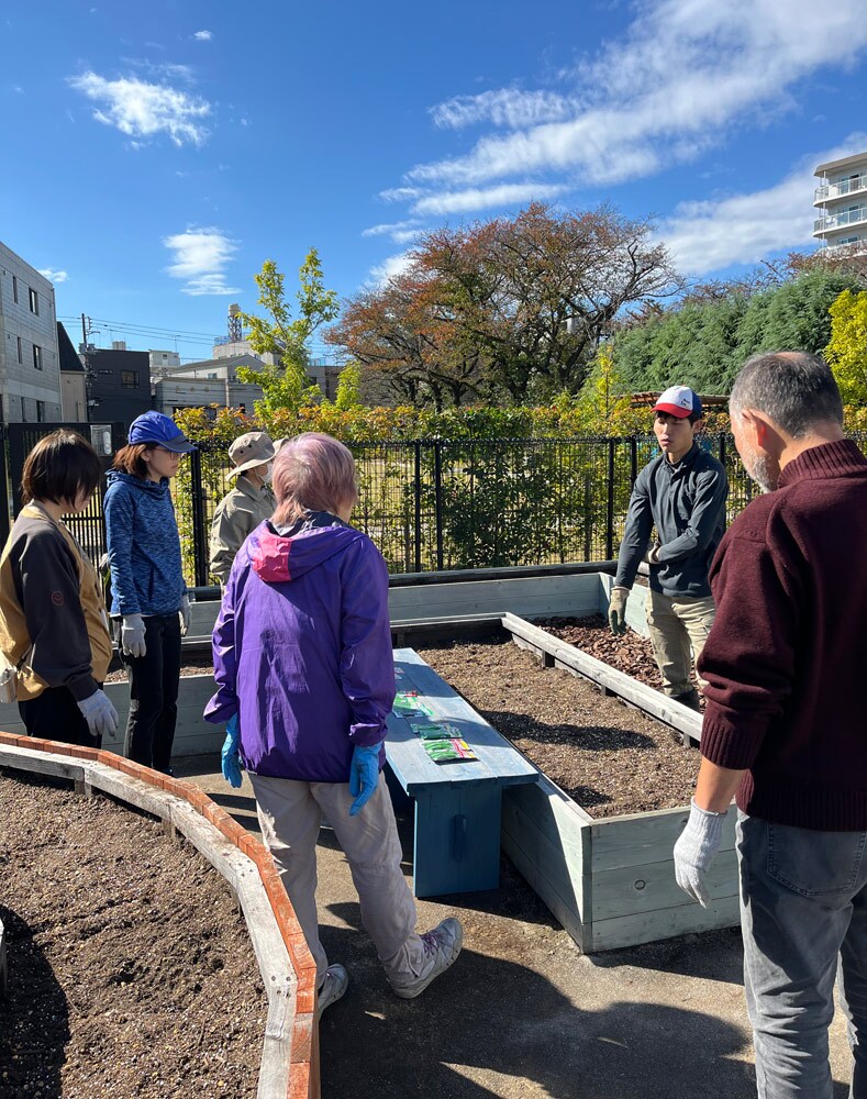 農業指導員の指導で種まきを開始。60歳代以上の参加者が中心ですが、子どもと一緒に参加している人もいるため、幅広い世代の交流の場となることが期待されます。