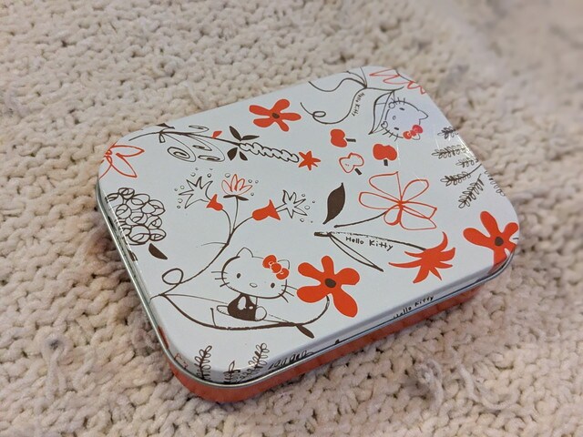 ハローキティの線画フラワー柄があしらわれた缶ケース