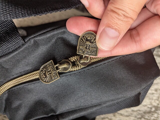 アンティークゴールド調のダブルファスナー引き手。ロゴ模様入り