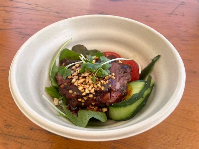 赤坂四川飯店の口水牛肉（よだれ牛）。白い器にルッコラやトマト、きゅうりと共に牛肉が盛られ、砕いたナッツと濃厚なタレがかかっている