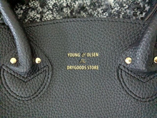 ブラックのレザー調バッグ正面の箔押しロゴアップ。YOUNG & OLSEN The DRYGOODS STOREの文字がゴールドで入っている