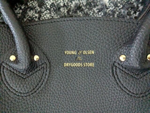 ブラックのレザー調バッグ正面の箔押しロゴアップ。YOUNG & OLSEN The DRYGOODS STOREの文字がゴールドで入っている