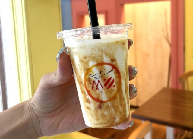 じゃばらとフローズングリークヨーグルト シェイクを手に持った様子。カラフルな店内が背景