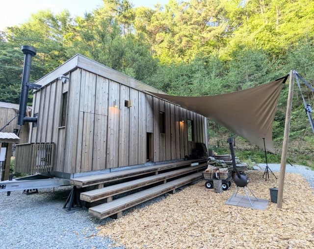 森に囲まれたEarthboat Ueda Onsenの客室棟外観とタープ