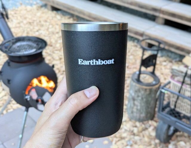 焚き火の前でEarthboatのロゴ入りタンブラーを手にしている様子