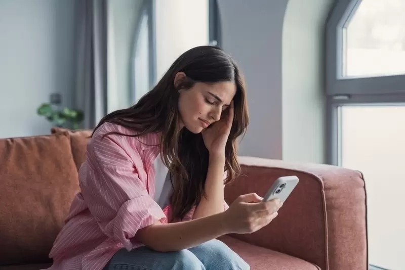 スマートフォンを見ながら考え込む女性