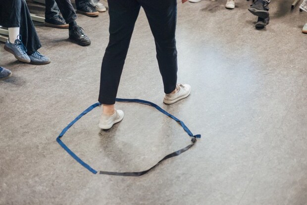 テープを円形に貼った中を通る人の足