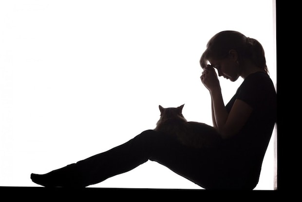悲しむ人と膝の上に乗る猫のシルエット