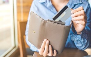 カードをグレーブラウンの長財布にしまう女性