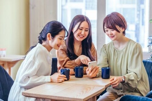 女性3人がカフェでスマホを見て話す様子