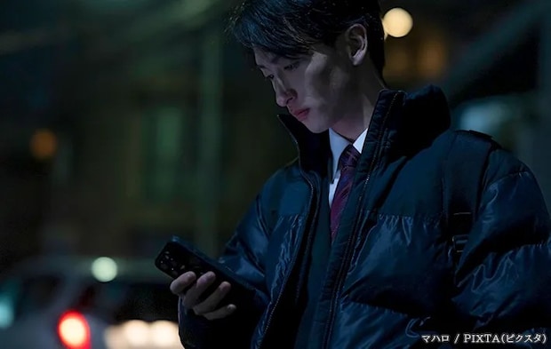 夜道でスマホを見る男性の写真