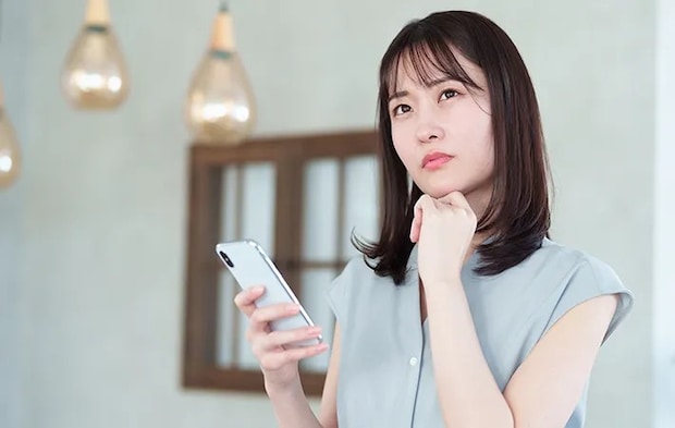 スマホをもって悩む女性の写真