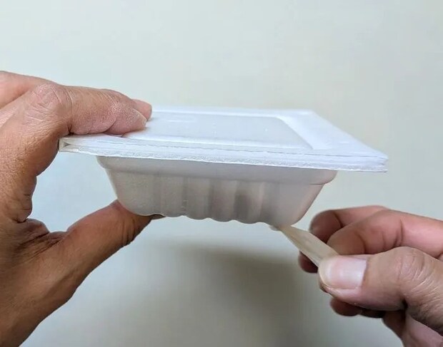 穴を開けた納豆パックの端からフィルムを取り出している様子（撮影：grape編集部）