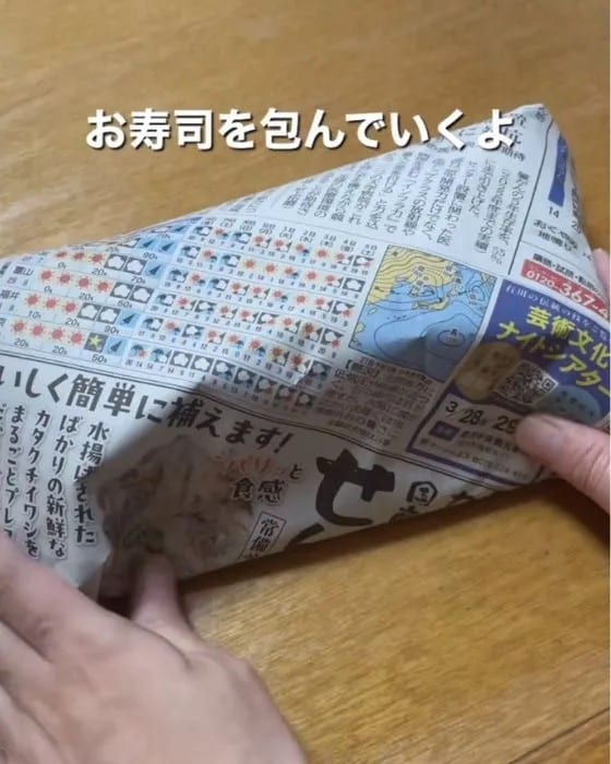 お寿司のパックを新聞紙で包んでいる様子