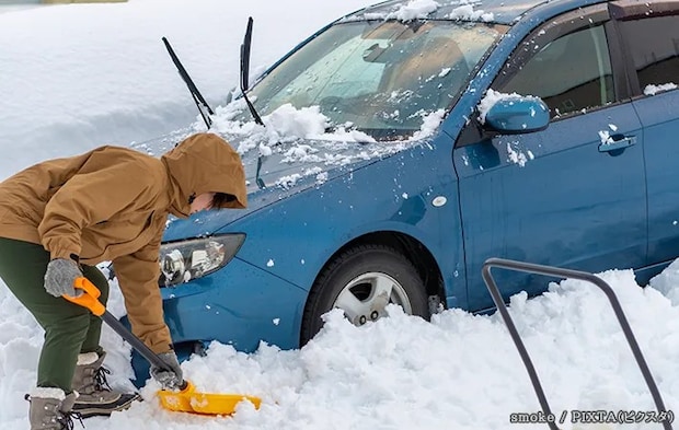 車の周りを雪かきする女性の写真
