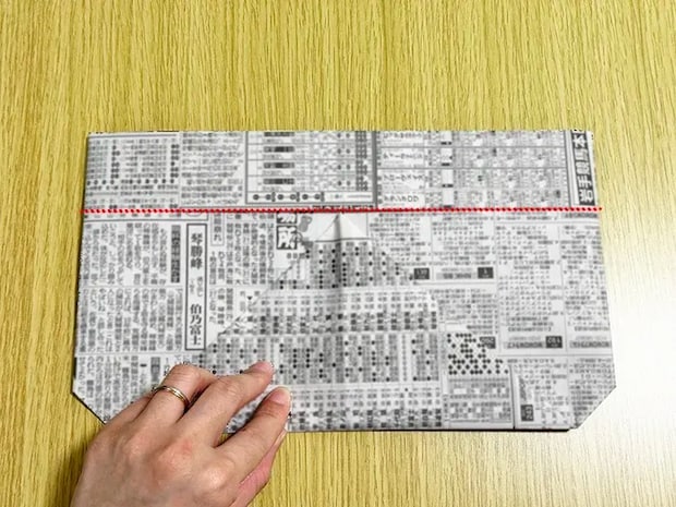新聞紙の上の線に頂点を合わせるように、下の角を三角に折った画像（撮影：grapeライフハック編集部）