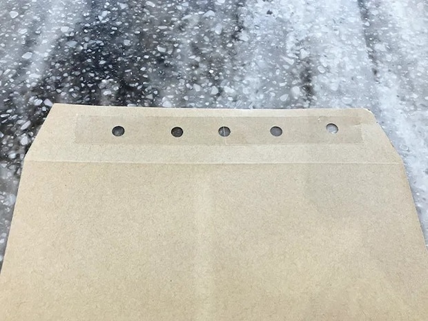 封筒に穴開けパンチで穴を開け、セロハンテープを貼った場面（撮影：grapeライフハック編集部）