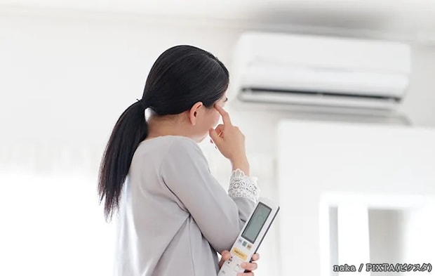 エアコンの前で困っている女性の写真