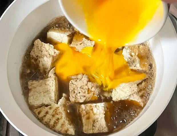 焼き豆腐を煮込む鍋に溶き卵を入れる写真（撮影：grapeフード編集部）