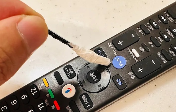 ヘアピンの先にティッシュを巻いてテレビリモコンのボタンの隙間を掃除している写真（grapeライフハック編集部）