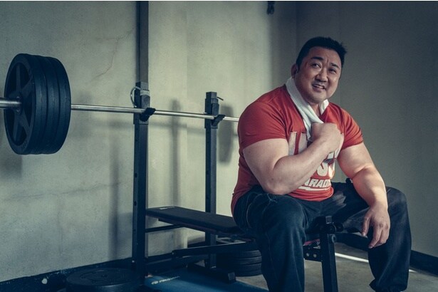 ドンソクがトレーニングマシンに腰かけ笑顔を見せる様子