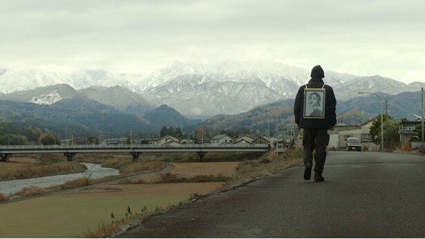 果てしなく続く山景色のなか、妻の遺影を手にさまよう信治