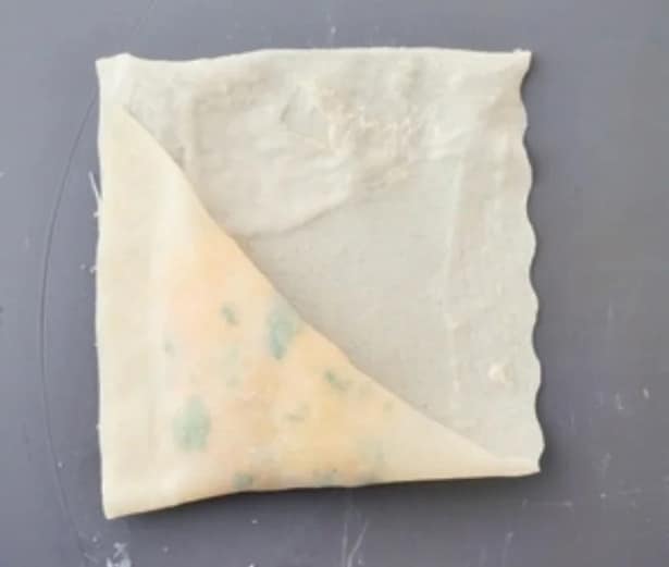 『三角春巻きの包み方』②　奥側に折り畳み、さらに三角形になるように折り、重なった辺どうしを指で押さえて密着させる。