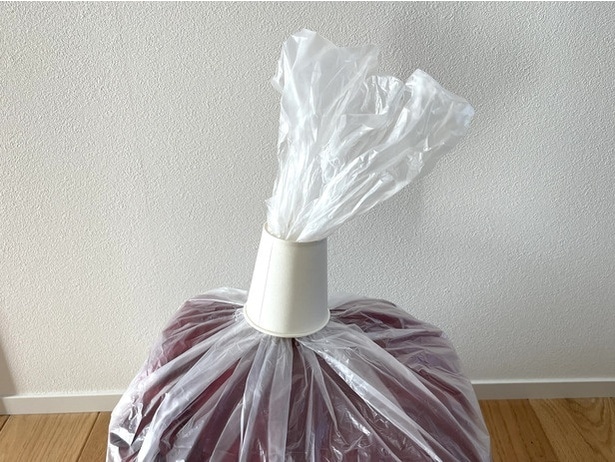 圧縮したい服を入れたビニール袋の口に紙コップを通す（▶次へ）