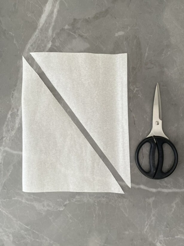 三角形が2枚できるよう、クッキングシートを斜めにカット（▶次へ）