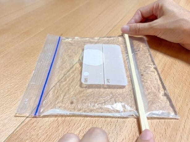 水の入ったジップ付き保存袋を割りばしで挟む（▶次へ） 