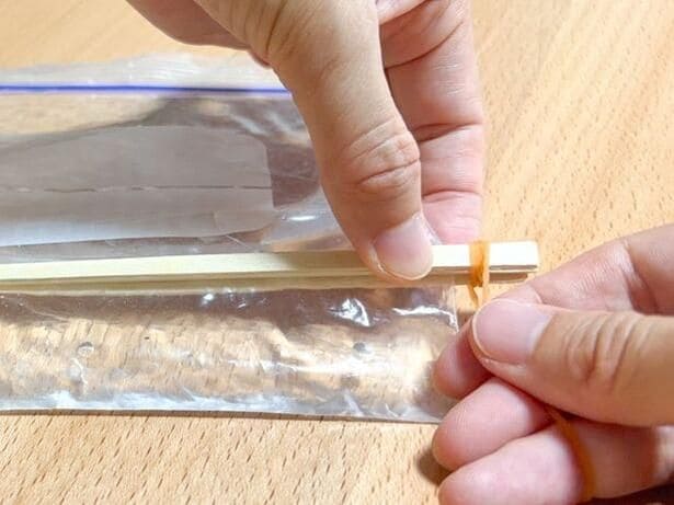 割りばしの両端を輪ゴムで固定する（▶次へ） 