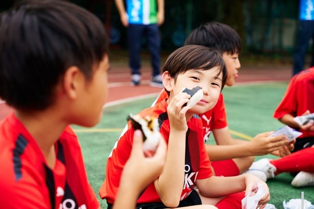 差し入れのおむすびを頬張る東京三育小学校サッカー部の子どもたち