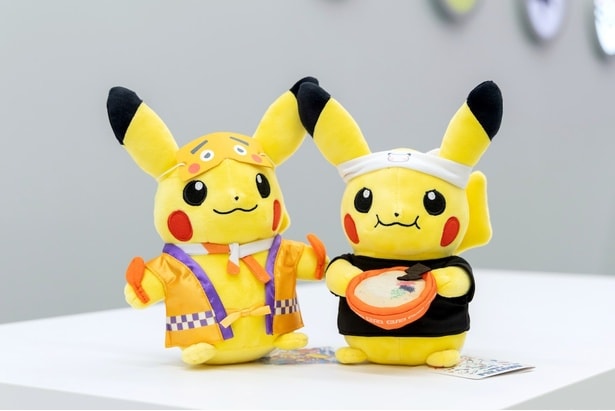 ラーメン店主風の衣装を着せてもらったピカチュウと、にわか面をつけてもらったピカチュウのぬいぐるみ