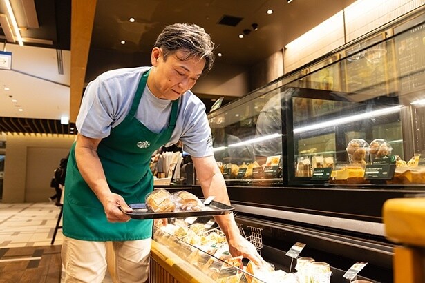 開店前、レジ前の陳列棚にフードを並べるトージさん