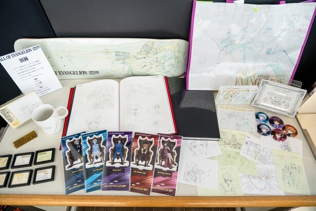 会場限定の主なオフィシャルグッズ。缶バッジセット(2750円・右)、展示原画をあしらったトレーディングマグネット(660円・左下)、スケートボードデッキ(1万4850円・左上)、40枚入りのポストカードBOX(7700円・右下)など魅力的なアイテムがそろう