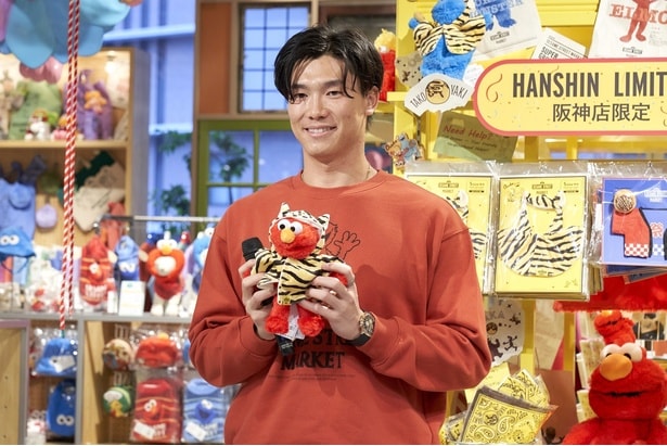 阪神梅田本店限定のトラコスチュームを着たエルモを手に取る湯浅選手。「来年のユニフォームもこんな柄で」とまさかの提案