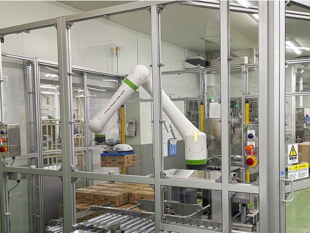 白い大きなアームが、パウチの梱包された段ボール箱を積み重ねていく