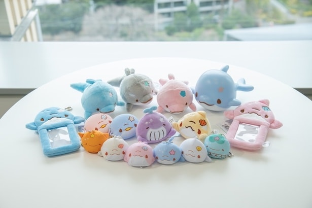 「ぬいぐるみ」(1870円/左奥)、「ルームランプ」(2980円/右奥)、「カードホルダー」(あおいるか・ぴんくいるか各1650円/両サイド)、「シリコンケース」(あおいるか・ぴんくいるか各1078円/中列左)、「フェイスマスコット」(くーみん・あるる各1320円/中列右)、「ビーズマスコット」(8種各990円/前列)