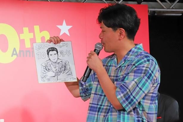 贈られた似顔絵を眺める阪本さん。ステージには「すげえ!」「かっこいい」と声が飛び交っていた