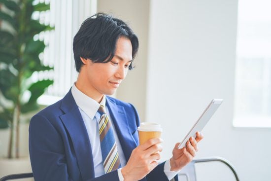 昼休憩中にタブレットを見ながらコーヒーを飲む