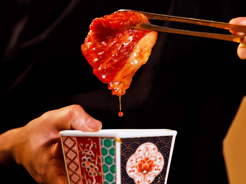 六本木『焼肉 東京24区』の肉をタレにつけている様子