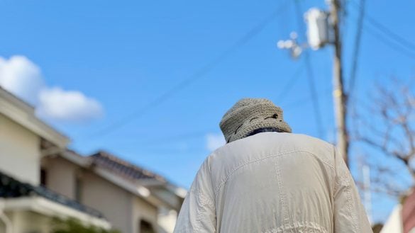 青空の下の住宅地を歩く高齢女性の後姿