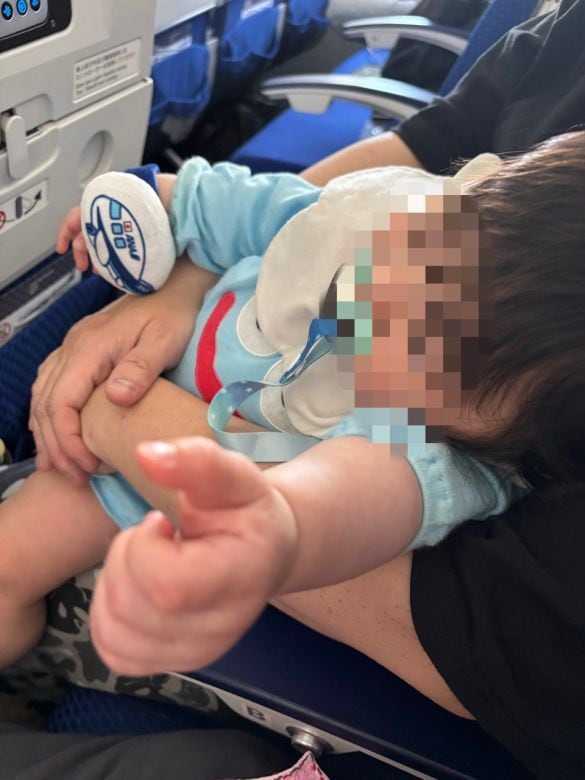  飛行機の中で爆睡中。腕にはもらった飛行機のオモチャ