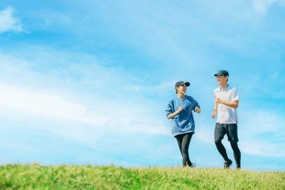 青空の下でジョギングをする笑顔の日本人男女