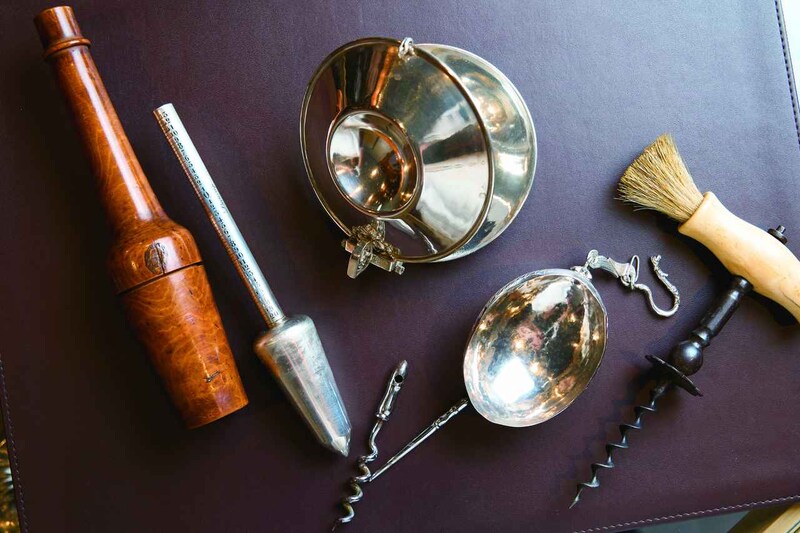 画像: セラーに展示されているワイングッズコレクション。二枚貝のようになっているダブルのタストヴァンは19 世紀のアンティーク。ボルドーのワイン商がロンドンにワインを輸出する前後にワインがすり替えられていないかを、比べてチェックするためにダブルになっているとか