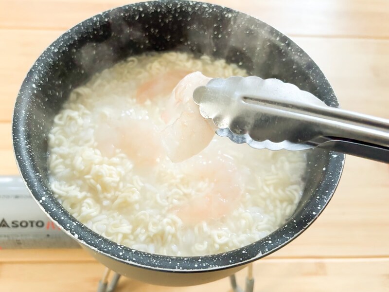 インスタント麺を投入したら軽くかき混ぜ、スライスしたむきエビ、ベーコン、しめじなどの具材を投入します